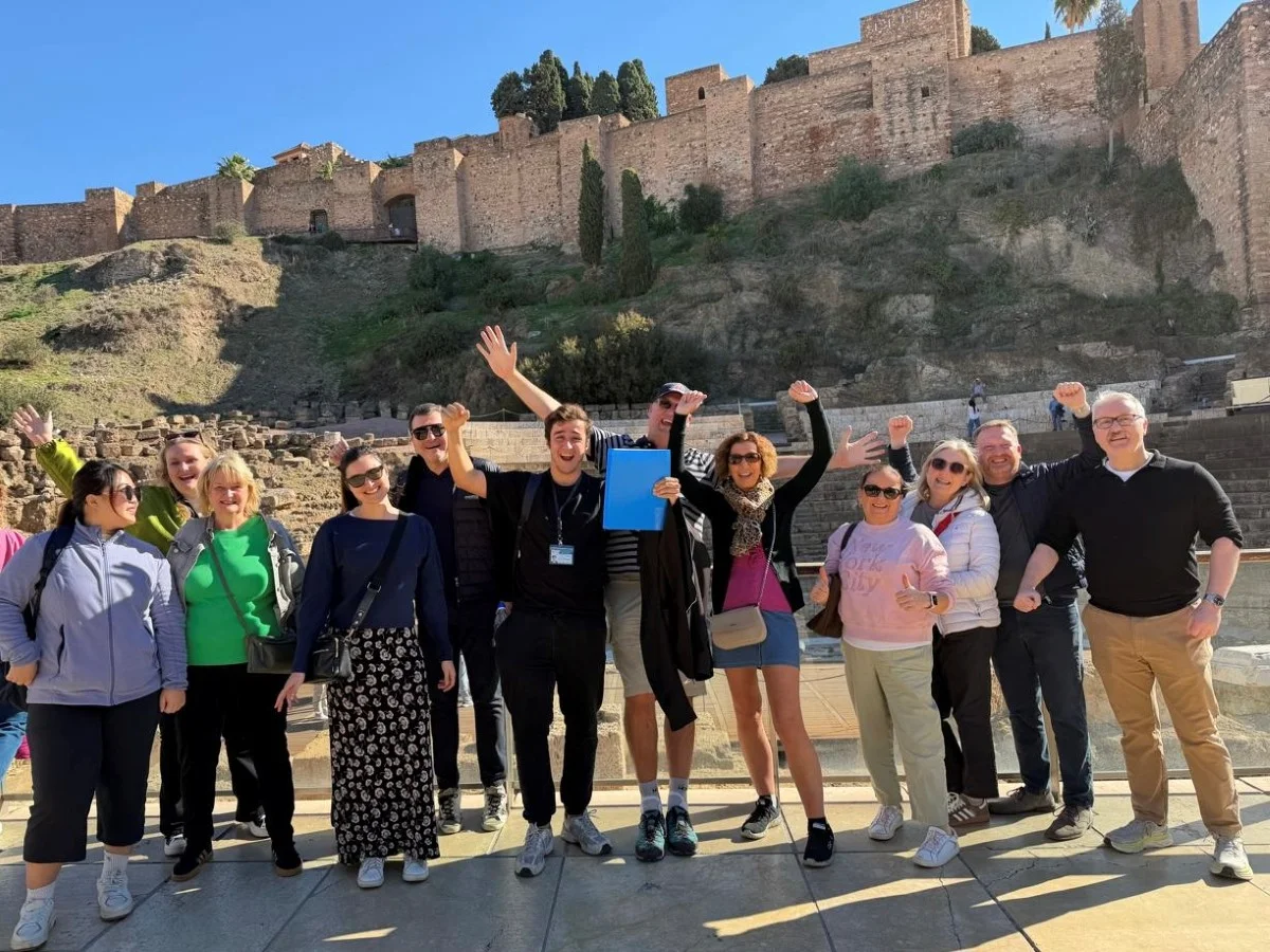Guided free tour group with guide having fun in Málaga historic centre with the alcazaba and the roman theatre in the background on a good day with blue sky