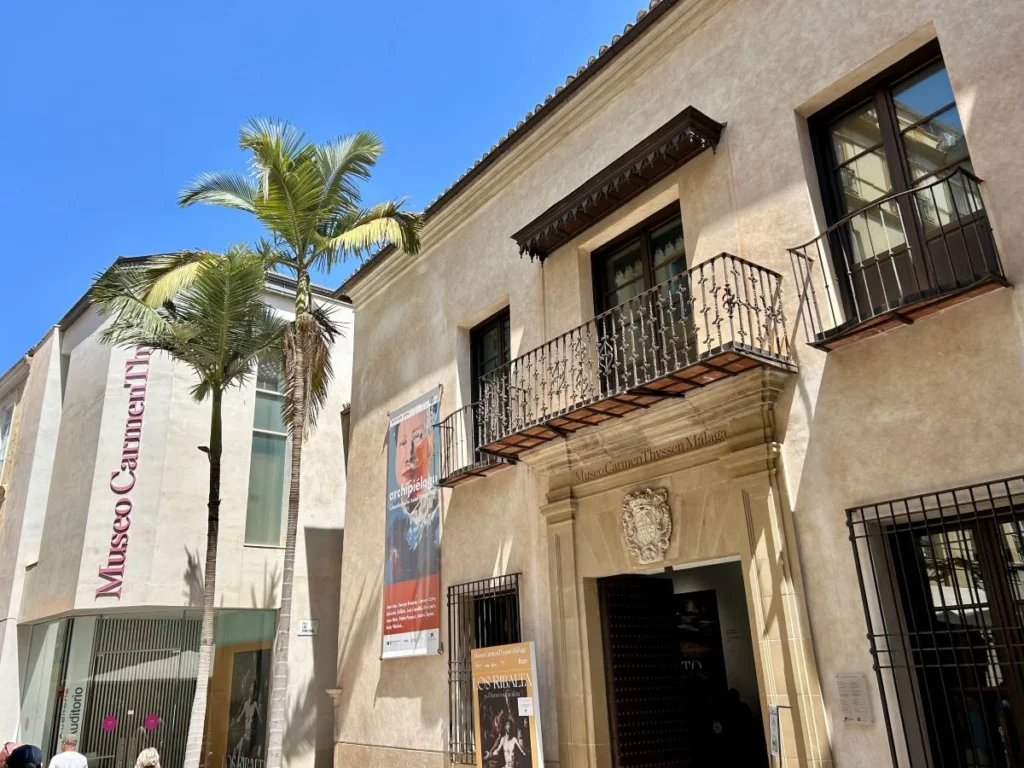Exterior facade of Museo Carmen Thyssen Málaga with exhibition posters and palm tree in the city centre