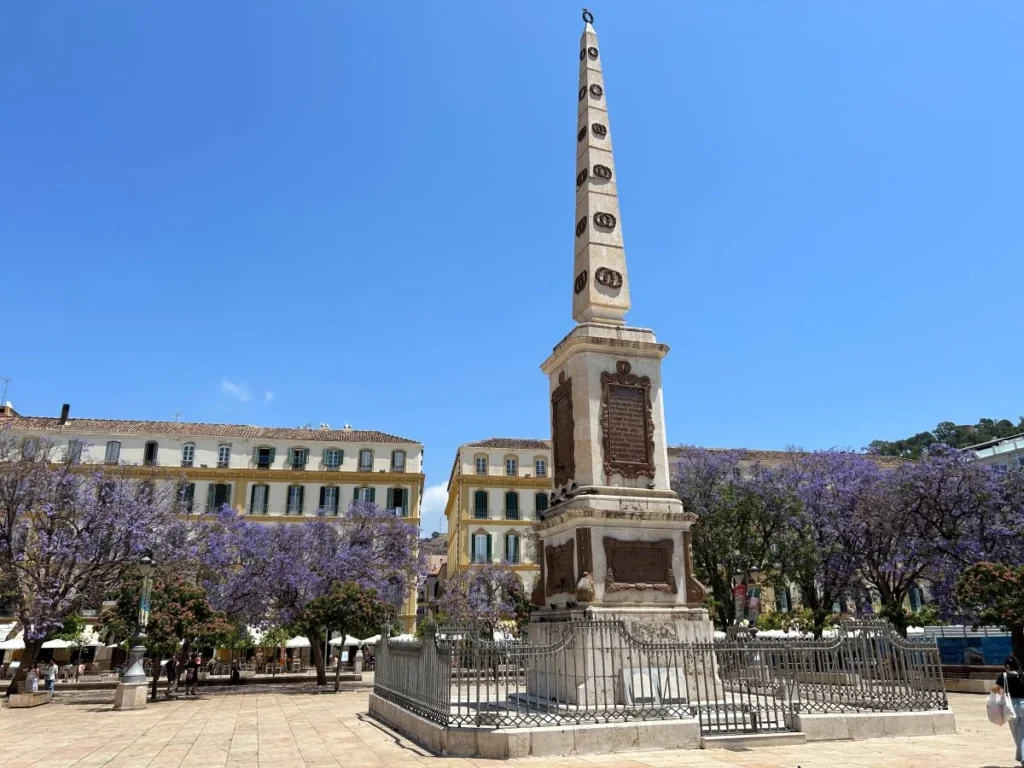 Plaza de la Merced obelisk surrounded by blooming jacaranda trees in Málaga