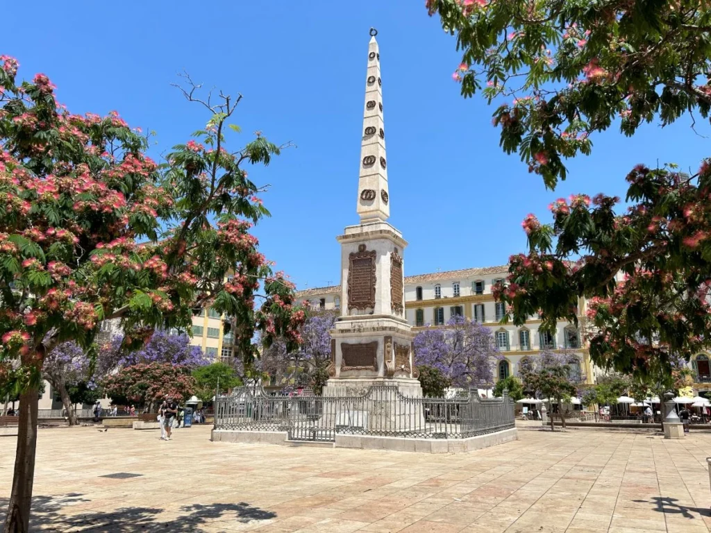 Colourful trees on Plaza de la Merced in Málaga with the Casa Natal de Picasso birthplace building and central obelisk on a sunny day