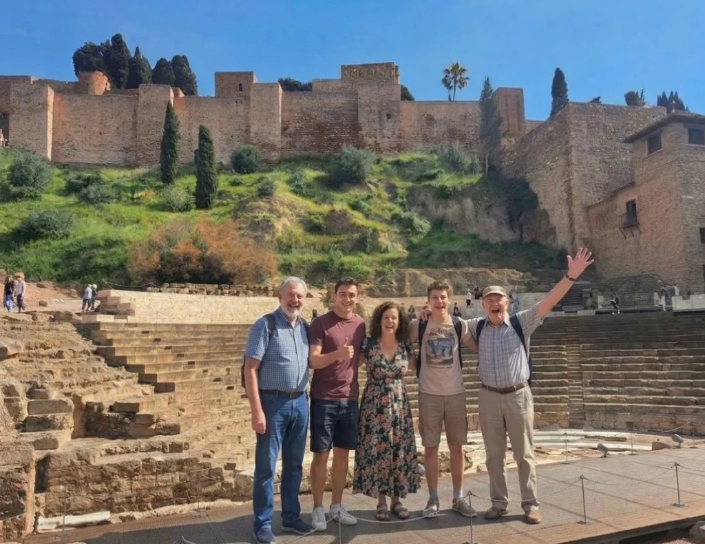 Tour group having fun with local expert guide in the Roman Theatre of Málaga during a private tour through the historic centre with the alcazaba in the background