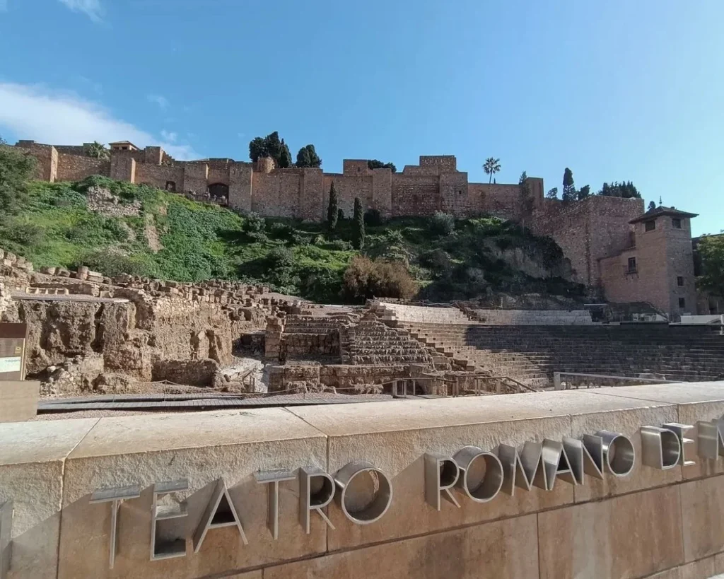 Ancient Roman theatre ruins in Málaga with the Alcazaba fortress rising behind them on a sunny day