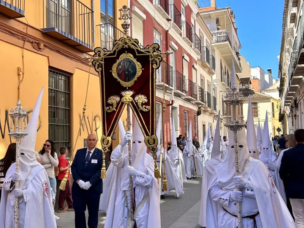Semana Santa procession easter with hooded penitents carrying a religious banner through Málaga streets in spring