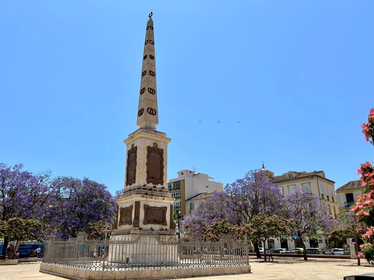 Obelisk monument in Plaza de la Merced surrounded by blooming jacaranda trees, near Pablo Picasso's birthplace in Málaga