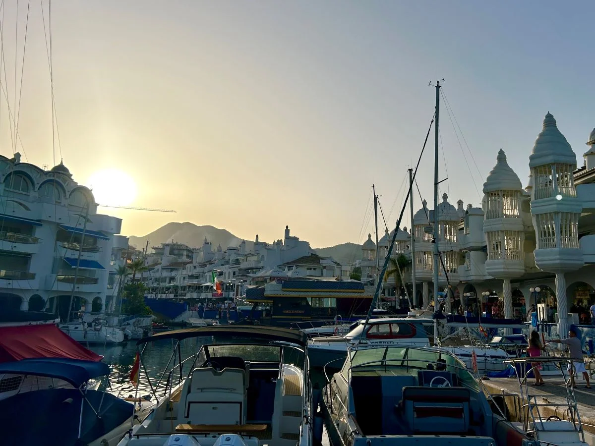 Sailboats and yachts moored at Puerto Marina Benalmádena at golden hour, with the Ferris wheel visible in the distance