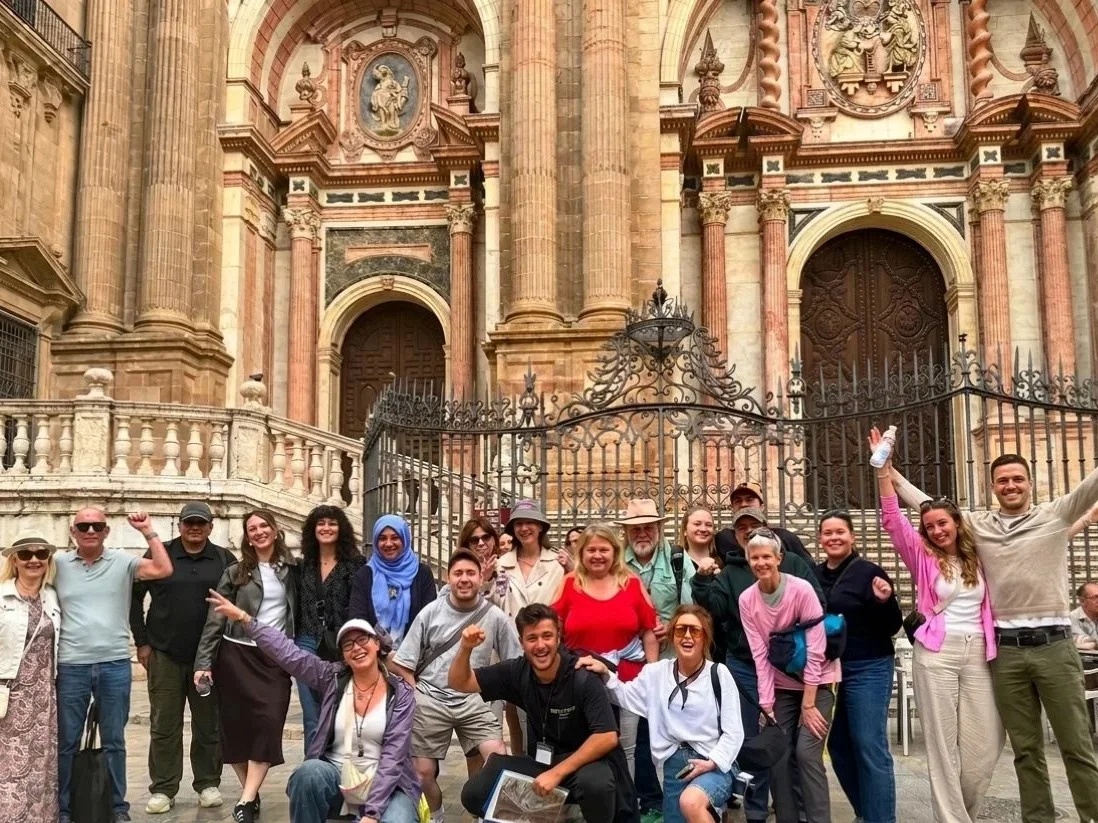 Group with guide during free walking tour of málaga with cathedral in the background having fun